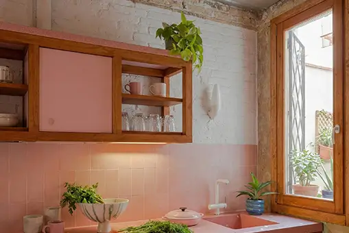 Renovated Barcelona kitchen with pink cabinets and exposed brick Apartment Renovation Barcelona pink kitchen with exposed brick wall, wooden window frame and indoor plants
