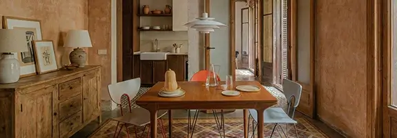 Warm Barcelona dining room with vintage tiles and wooden furniture Renovated Barcelona loft dining room with wooden table, mixed chairs, patterned vintage floor tiles and open doorway to kitchen and balcony