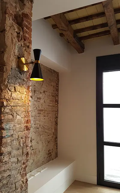 Detail of exposed brick wall, modern wall light and window in renovated apartment showcasing home renovation services Barcelona by Revive Quality