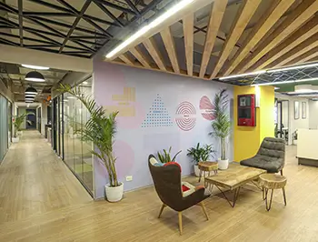 Modern Eixample office with lounge area and glass meeting rooms Renovated Eixample office space with wooden flooring, colorful accent wall, lounge seating, indoor plants and corridor of glass-walled meeting rooms