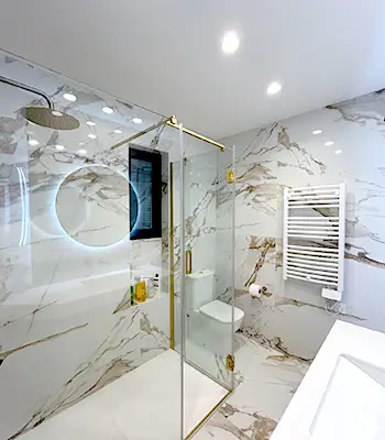 Small Eixample bathroom with marble-effect tiles and glass shower Compact Eixample bathroom from our Renovation Projects Barcelona portfolio, with marble-effect walls, walk-in glass shower, gold fixtures and modern vanity