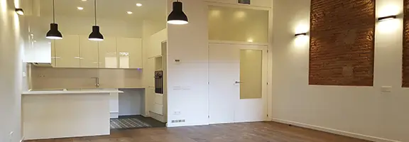 Renovated El Born apartment with open-plan kitchen and exposed brick wall Renovated El Born Barcelona apartment with open-plan white kitchen, pendant lights and exposed brick feature wall