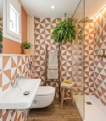 Colorful El Born bathroom with geometric tiles and walk-in shower Heritage-style El Born bathroom renovation with orange and white geometric tiles, wall-hung toilet, walk-in glass shower and hanging plants - by Revive Quality