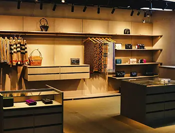 Gràcia boutique shop interior with custom wooden displays Renovated Gràcia retail shop with wooden shelves, hanging rails, glass display counters and warm accent lighting