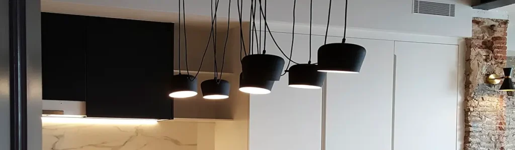 Black pendant lights in renovated Gràcia open-plan kitchen Close-up of black pendant lights above a renovated Gràcia kitchen with white cabinets, marble backsplash and exposed brick wall