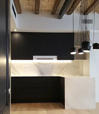 Compact modern Gràcia kitchen with black cabinets and marble peninsula Space-optimized Gràcia kitchen with black upper cabinets, white marble backsplash and peninsula, pendant lights and exposed wooden ceiling beams