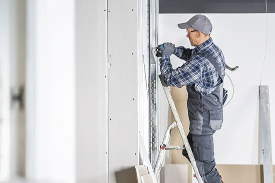 Insulation specialist in Barcelona installing interior wall panels on a ladder during home renovation