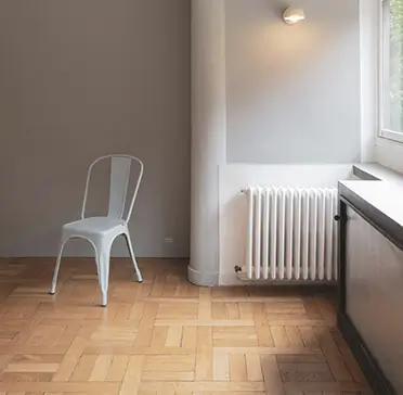 Minimalist room with light parquet flooring Bright minimalist room with light wood parquet flooring, metal chair and radiator by the window