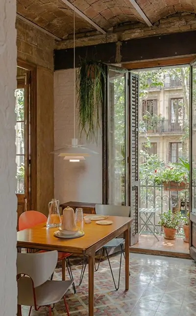 Barcelona apartment dining area with balcony and patterned floor tiles Renovation Projects Barcelona showcasing a renovated dining room with original patterned floor tiles, wooden table, modern chairs and balcony overlooking a leafy street - by Revive Quality