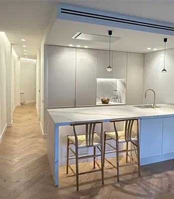 Modern Eixample kitchen with island and herringbone flooring Renovation Projects Barcelona featuring a modern Eixample kitchen renovation with white island, bar stools, integrated cabinets and herringbone wood flooring
