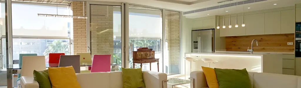 Bright open-plan living room and kitchen in renovated Sant Antoni home Sant Antoni heritage home renovation with open-plan living room, colorful cushions, dining area and modern kitchen island with pendant lights