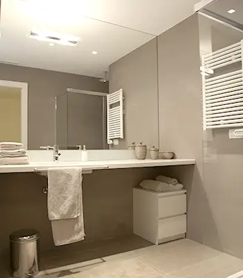 Elegant Sarrià bathroom with large vanity and walk-in shower Luxury Sarrià bathroom renovation with wide countertop vanity, large mirror, walk-in glass shower and neutral stone-style finishes