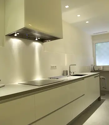 Bright minimalist Sarrià kitchen with sleek white cabinets Luxury Sarrià Barcelona kitchen with long white cabinets, integrated cooktop, stainless steel hood and modern recessed lighting